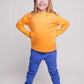 A blonde haired girl wearing an orange jumper and blue joggers - Hues Clothing