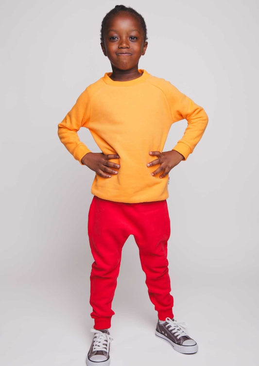 A boy wearing an orange jumper and red joggers - Hues Clothing