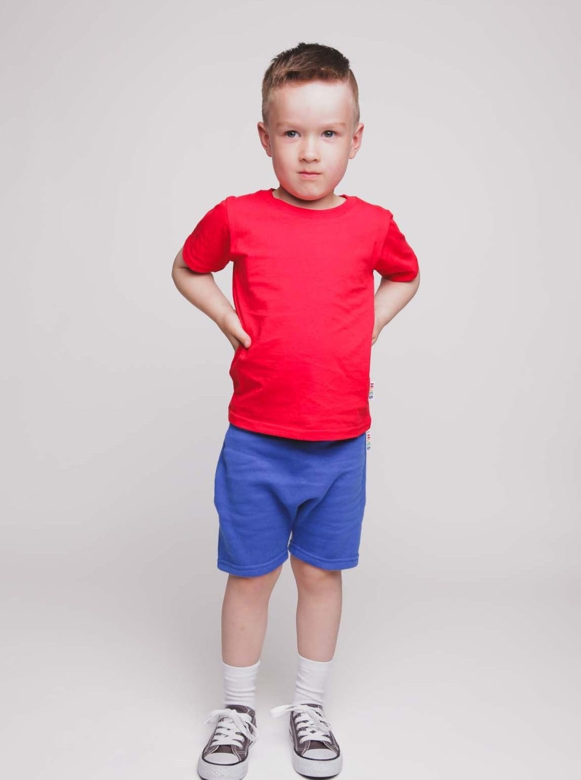 A boy with a short a haircut wearing a red t-shirt and blue shorts - Hues Clothing